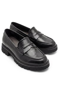 Ζευγάρι μαύρα δερμάτινα loafers με χοντρές σόλες με αυλακώσεις και διακοσμητικό λουράκι στην κορυφή, ελαφρώς γερμένα προς τα δεξιά σε λευκό φόντο.