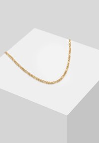 Goldene Halskette mit verdrehten Gliedern und glatter Oberfläche, präsentiert vor einem hellen Hintergrund auf einem geometrischen Podest.