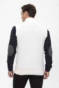 Chaleco sin mangas blanco texturizado con dobladillo de punto, llevado sobre una camiseta de manga larga negra con parches grises en los codos.