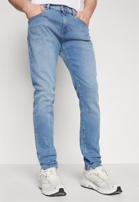 Ljusblå jeans i denim med slim fit, femficksdesign och kontrasterande sömmar, tillsammans med grå och vita träningsskor.