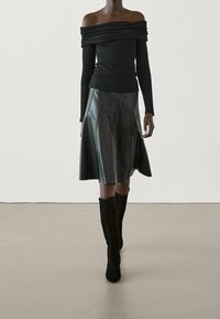 Top nero senza spalline con scollatura drappeggiata, abbinato a una gonna in pelle scura al ginocchio con pieghe verticali e texture. Stivali neri al ginocchio.