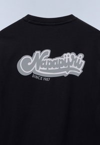 Μαύρο ύφασμα με μεγάλο γκρι στυλιζαρισμένο λογότυπο "Napapijri" και μικρότερο κείμενο "Since 1987" κάτω από το λογότυπο.