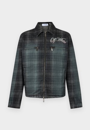 Mand iført sorte solbriller, gradienttern jakke med teksten "Off-White", grå skjorte, sorte cargobukser og sort-hvide sneakers, stående.