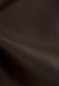 Materiale in pelle marrone con texture, finitura morbida e leggermente lucida, caratterizzato da un delicato motivo a granuli e curve morbide.