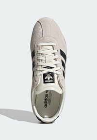 Gray suede sneaker with white laces, black side stripes, and a black logo patch. Features a textured rubber sole and padded collar.