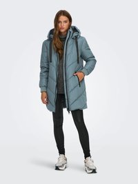 Lyseblå boblejakke med hette, med quiltet design, grå detaljer og glidelåslommer, kombinert med svarte leggings og joggesko.