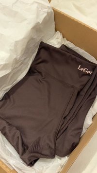 Σκούρο καφέ ριμπ αθλητικό σορτς με λογότυπο "LeGer", διπλωμένο μέσα σε χαρτόνι επενδυμένο με λευκό χαρτί περιτυλίγματος.