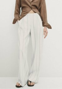 Pantalon blanc à jambes larges avec des rayures ondulées verticales grises. Associé à une chemise marron boutonnée, offrant une coupe décontractée et une texture lisse.