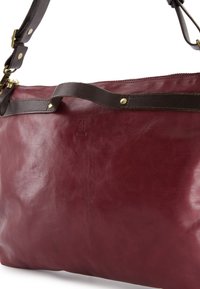 Diep rode leren schoudertas met een donkerbruine strap en messing hardware, close-up die de textuur en het ingedrukte logo laat zien.