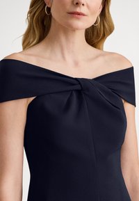 Μπλε σκούρο φόρεμα με έναν ώμο, με λεπτομέρεια διπλωμένου κόμπου στο ντεκολτέ, με λεπτή υφή και εφαρμοστή σιλουέτα.
