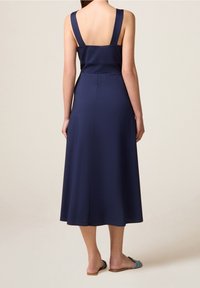 Robe sans manches bleu marine avec des bretelles larges, corsage ajusté et jupe évasée midi. Tissu doux avec un léger brillant, design minimal.