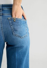 Heledad teksased heledas sinises, sirge lõikega, seljal taskuga, millel on hõbedane logo aktsent ja peen kulumine.