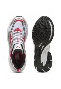 Chaussures de sport avec un dessus en maille blanche, des accents rouges et noirs, et une semelle en caoutchouc noir texturé présentant un motif distinctif.