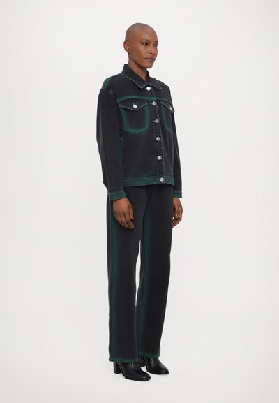 Veste en denim noire avec des accents verts, dotée de deux poches poitrine et de fermetures à boutons, associée à un pantalon noir assorti avec des bandes latérales vertes.