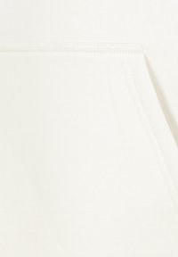 Heller beiger Stoff mit glatter Textur und einer Fronttasche. Verfügt über Nähdetails entlang der Kanten, die ein einfaches, funktionales Design schaffen.