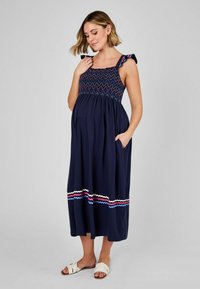 Abito da maternità con un corpetto blu scuro, parte superiore arricciata e spalline con volant; presenta accenti zigzag colorati e una gonna lunga e fluida con tasche.