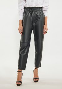 Sorte faux læderbukser med høj talje, elastisk taljebånd og tapered ben; glat tekstur og minimalt antal sømme for et elegant udseende.