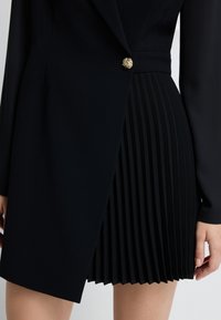 Czarna sukienka z dopasowanym topem i plisowaną spódnicą. Złoty guzik na wysokości talii. Gładki materiał o strukturalnym fasonie.