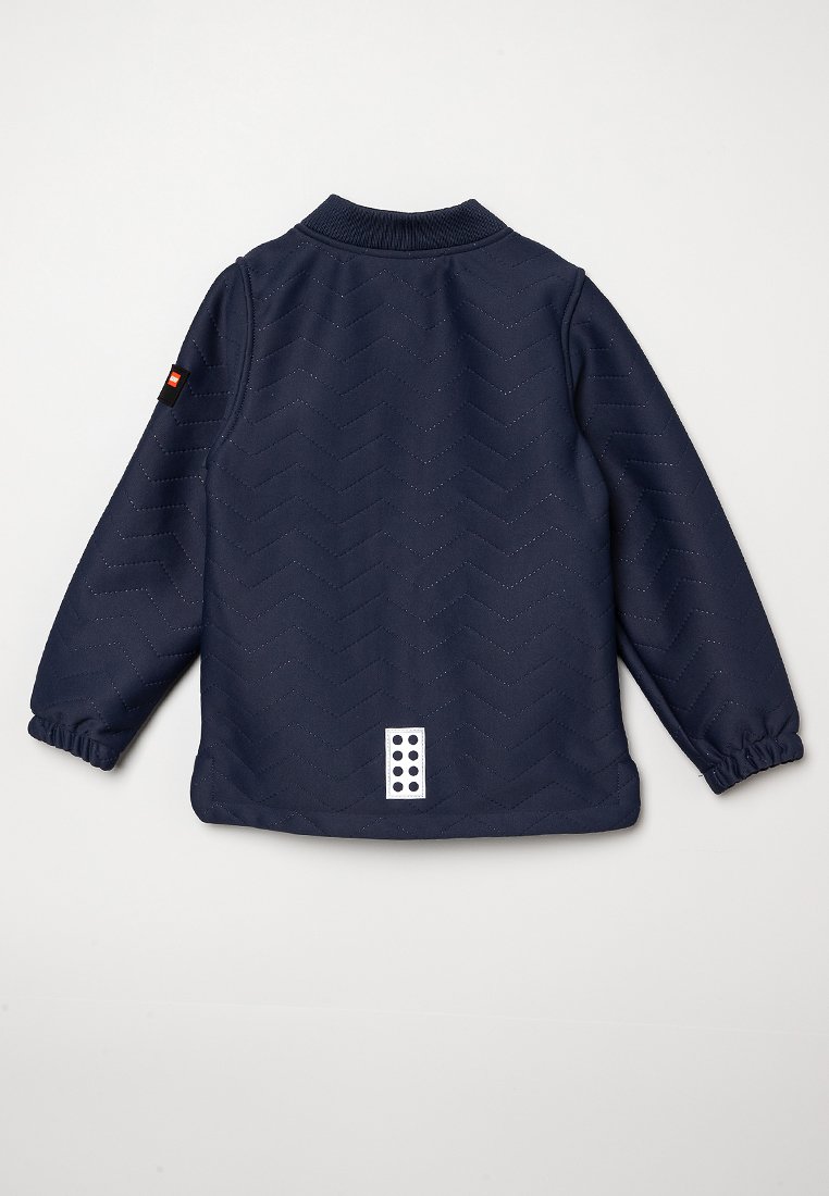 Giacca navy trapuntata con colletto a coste, polsini elasticizzati, texture a zigzag e un'etichetta bianca con ritagli tondi sul retro.