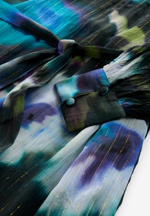 Višenamjenska haljina u više boja koja sadrži nijanse plave, zelene i ljubičaste, s zlatnim metalnim prugama i detaljem s vezanjem u struku. Rukavi bluze s dugmadi.