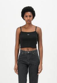 Black ribbed crop top with thin straps and a square neckline, featuring a small logo at the center and a fitted design. Worn with high-waisted dark jeans.