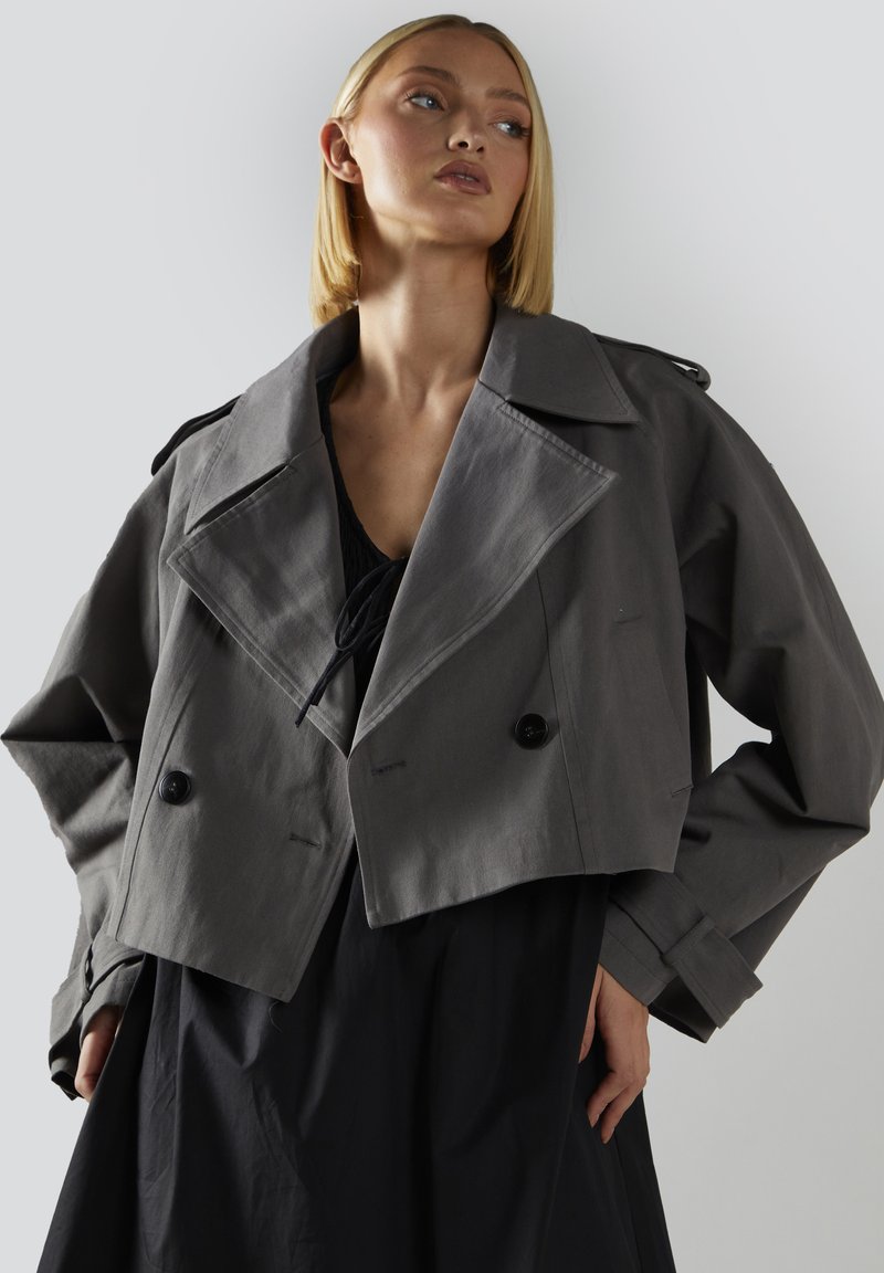 Lyhyt harmaa takki, jossa on suuri kaulus, kaksiriviset napit ja sivutaskut. Valmistettu silkkisestä materiaalista, jossa on kevyt kiilto.