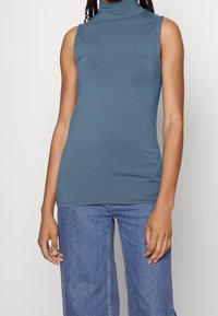 Top senza maniche in morbido tessuto blu. Texture liscia e design aderente, abbinato a jeans in denim chiaro a vita alta. Nessun motivo.