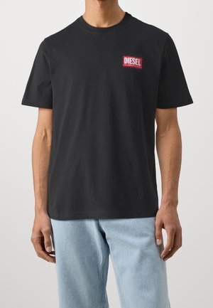 T-shirt en coton noir avec col rond, manches courtes, avec un logo "DIESEL" brodé en rouge sur la poitrine. Coupe ample, légèrement extensible.
