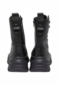 Botas de cuero negro hasta el tobillo con una suela de goma negra texturizada, correas decorativas, anillos de metal y cierre de cremallera en la parte posterior.