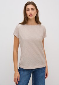 Top beige de manga corta con un patrón texturizado ondulado, escote redondo y un corte relajado, combinado con jeans de mezclilla azules.