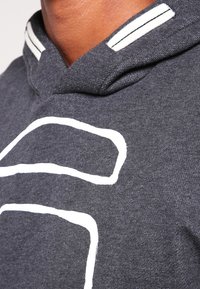 Felpa grigio carbone con design a contorno bianco, caratterizzata da uno stile a pullover e accenti striati sul bordo del cappuccio. Tessuto morbido.