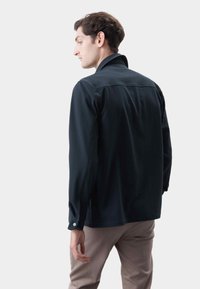 Camisa de botón azul marino oscuro con una tela texturizada, corte slim, cuello clásico, y mangas largas, con puños abotonados y cortes laterales.