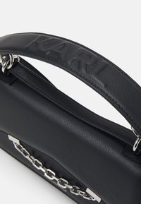 Borsa a mano in pelle nera con finitura testurizzata, dotata di una tracolla con logo impresso, dettagli in catena argentata e un design minimalista elegante.