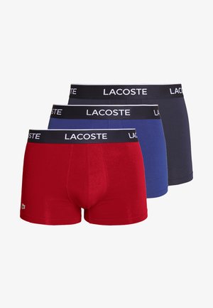 Tri parov Lacoste bokseric v rdeči, modri in mornarsko modri barvi. Vsak par ima črn elastičen pas z belim napisom "LACOSTE". Mehak material, prilegajoča zasnova.