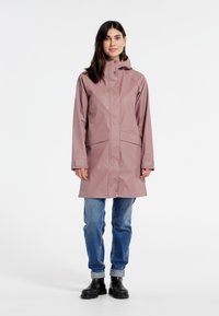 Rosa vattentålig regnrock med huva, långa ärmar, två framfickor och rak skärning, matchad med blå jeans och svarta stövlar.