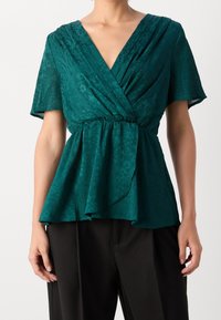 Blusa verde acqua con scollatura a V e maniche corte, caratterizzata da un design avvolgente, vita arricciata e orlo fluente, realizzata in tessuto testurizzato.