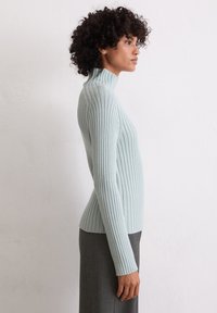 Hellblau gestrickter Rollkragenpullover mit langen Ärmeln, der mit texturiertem Stoff und einem figurbetonten Design überzeugt, kombiniert mit einem grauen Rock.