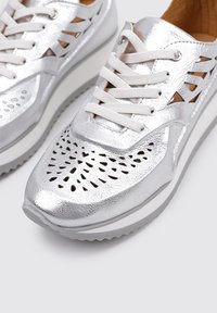 Zapatillas plates de metal con un diseño perforado, cordones blancos y una suela gruesa blanca. Superior texturizado y acentos recortados en los laterales.