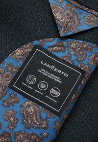 Niebieska tkanina w wzór paisley z czarną metką z napisem "LANČERTO", charakteryzująca się elastycznym materiałem, idealnym dopasowaniem oraz właściwościami zapobiegającymi gnieceniu.