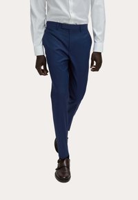 Granatowe spodnie z gładkiego materiału, o dopasowanym kroju i płaskim przodzie, zestawione z brązowymi skórzanymi butami oraz białą koszulą z guzikiem.