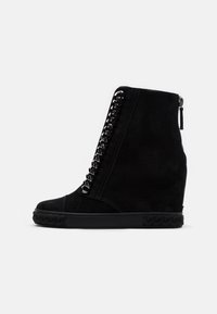 Czarne zamszowe sneakersy na koturnie z sznurowanym przodem, metalicznymi detalami w formie łańcucha, bocznym zamkiem błyskawicznym oraz teksturowaną gumową podeszwą z plecionym wzorem.