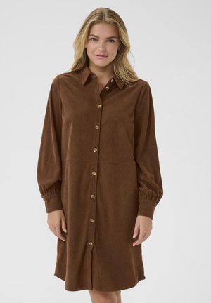 Brown corduroy shirt dress with long sleeves, button-up front, and gathered cuffs. Features golden buttons and a relaxed silhouette.