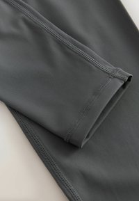Gray athletic leggings featuring a smooth, stretchy fabric, overlocked seams, and a folded cuff detail at the hem.