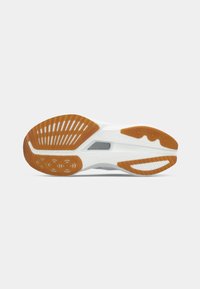 Semelle de chaussure de sport blanche avec des motifs de semelle orange et des accents gris, vue de dessous sur fond blanc.