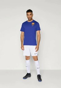 Modré tričko Nike s logem Barcelony, bílé šortky Nike, bílé ponožky a černé fotbalové kopačky. Jednoduchý design, hladká textura.