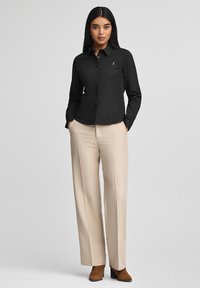 Camicia nera con bottoni, maniche lunghe e colletto a punta, abbinata a pantaloni beige con vita alta e stivaletti marroni con tacco.