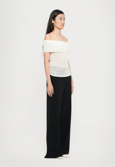 Valgest off-the-shoulder topist, millel on läbipaistev tekstuur, koos laia jalgadega mustade pükstega. Riietus on lõdva lõikega ja minimalistikus stiilis.