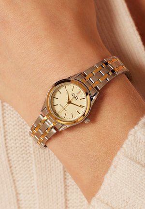 Gouden en zilverkleurige horloge met een ronde wijzerplaat, crèmekleurige wijzerplaat, minimalistische uurmarkeringen en een metalen schakelarmband. Waterbestendig.