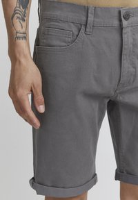 Gray cotton shorts with rolled cuffs, featuring front pockets and a button closure. Smooth texture and casual design.