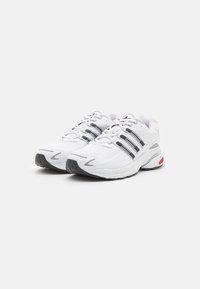 Weiße Sportschuhe mit schwarzen Akzenten, Schnürdesign, strukturierter Synthetik-Oberfläche, gepolstertem Schaft und Gummisohle mit roten Details.